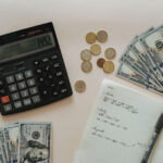A photo of a calculator, dollar notes, coins, and a notebook placed on a table