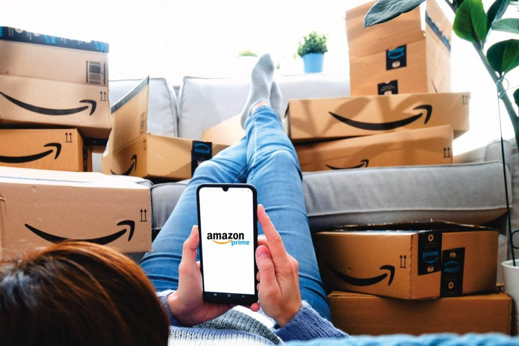 A woman sits with amazon boxes all around her while being logged onto amazon prime with her phone.