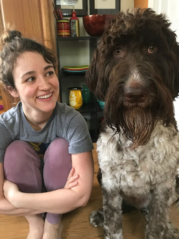 A young woman sits next to a large brown and white dog. 