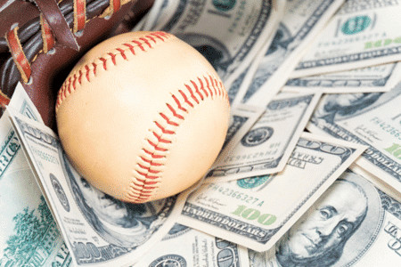 A baseball glove with a baseball and hundred-dollar bills, representing baseball player earnings