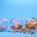 Three piggy banks against a light blue background, with varying amounts of coins in them.
