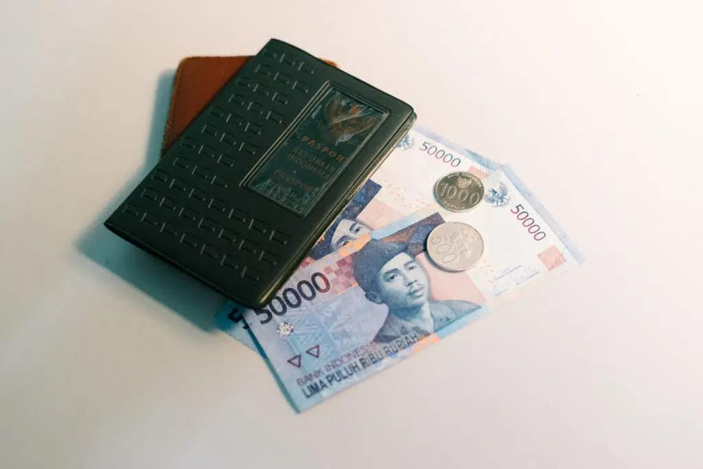 Close-up view of Indonesian Rupiah banknotes, a brown wallet, and a dark passport, illustrating the essential items needed when dealing with Indonesian money.