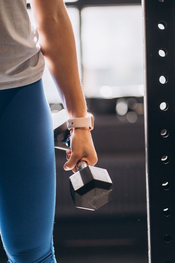 A gym training participant wearing a smartwatch and holding a dumbbell. Source: Freepik