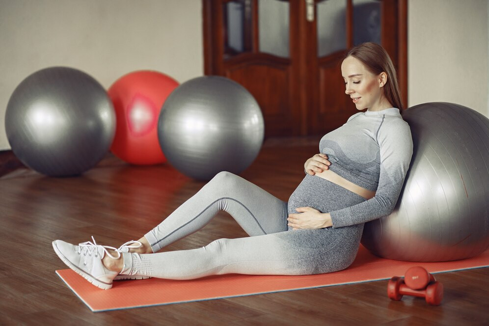 A pregnant woman sitting on a fitness mat with one big fitness ball and some more in the background. Source: Freepik