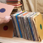 A person is selecting a vinyl record from a large collection in cardboard sleeves, showcasing the joy of discovery and the potential value of each record.