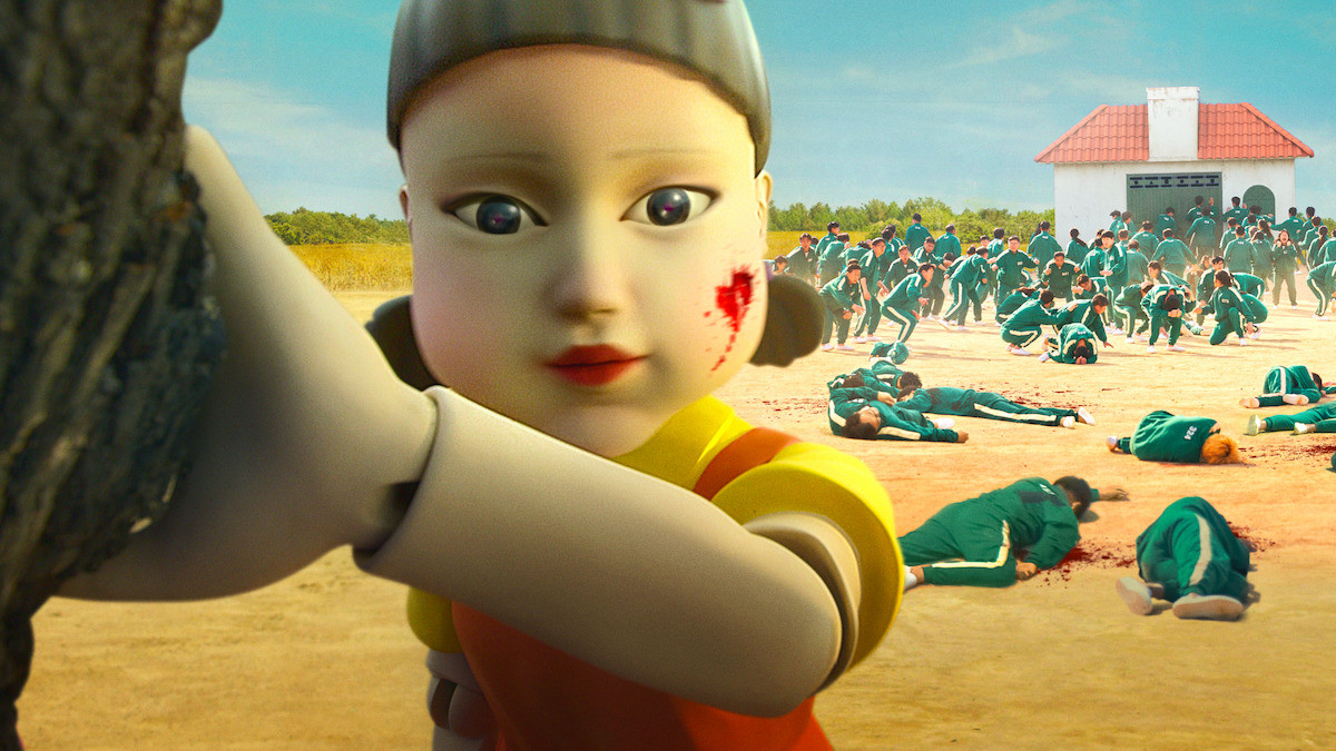 The giant doll from ‘Squid Game’ turns her head while people behind her wearing green sweat suits run away.