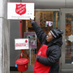 Bell ringer standing next to the red kettle of Salvation Army