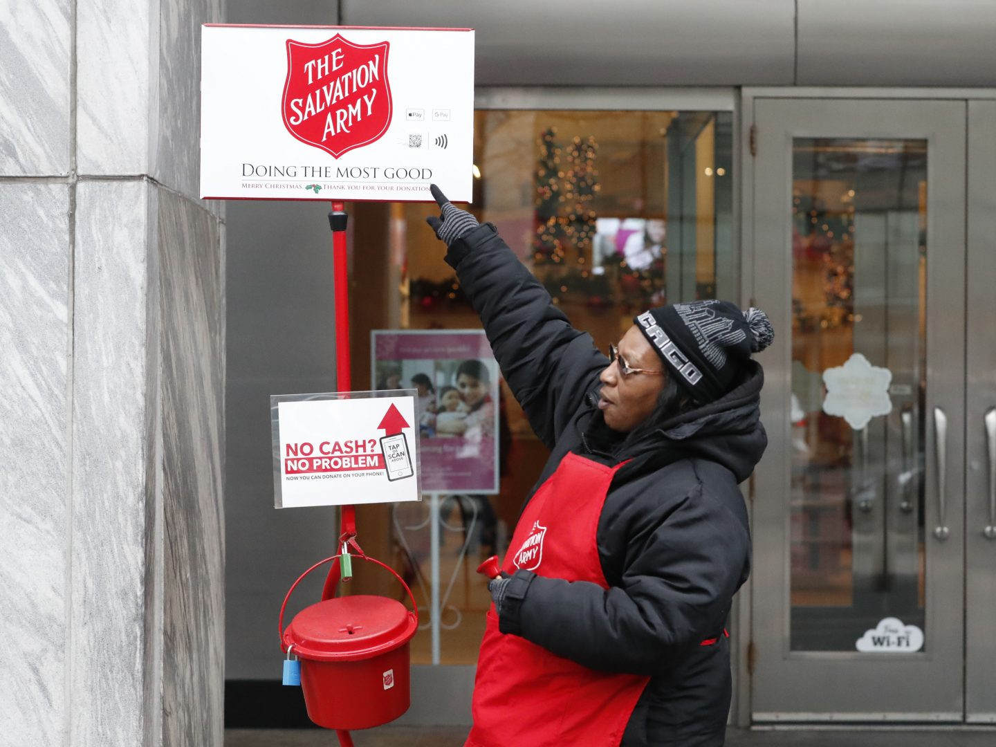 Bell ringer standing next to the red kettle of Salvation Army