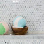 Two handmade bath bombs sit on a shower ledge
