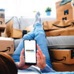 A woman sits with amazon boxes all around her while being logged onto amazon prime with her phone.