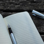 Person writing on a notebook with a pen on the table