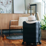 Still life of a black suitcase with a straw hat in the living room of an apartment. Travel and vacation concept