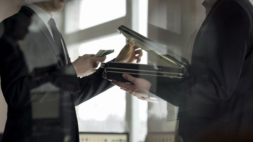 Money Laundering - Image of a man opening a case and holding several bank notes