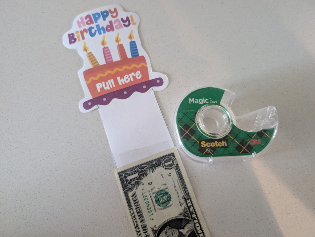 A close-up of taping the first dollar bill to the end of a birthday pull tab