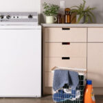 The speed queen washer next to a counter with a basket of laundry supplies near it on the floor.